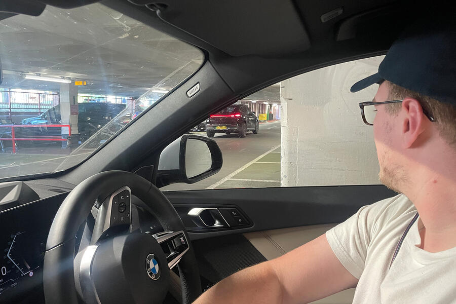 نمای عقب بی ام و ۱۲۰ در محیط شهری بی ام و سری ۱ در پارکینگ با رنگ خاکستری آسمانی